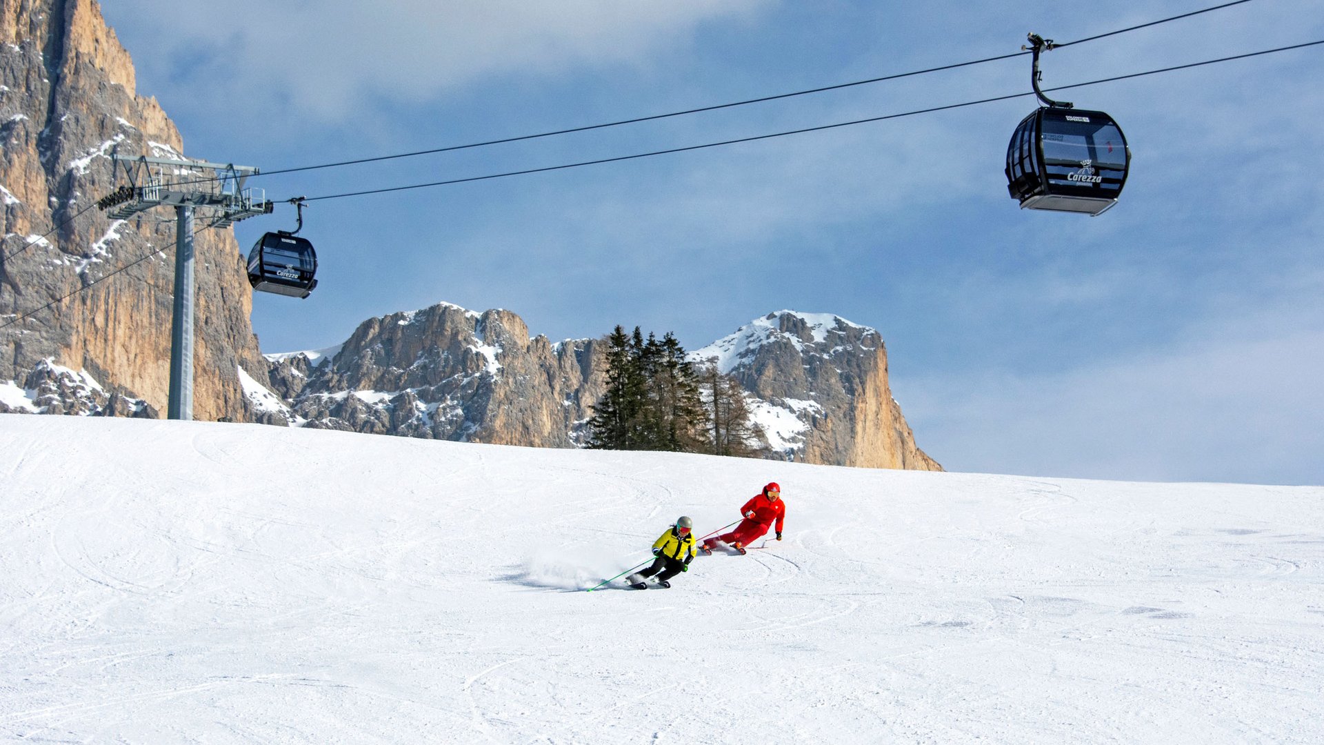 Sciatori su pista innevata con cabine della funivia e montagne sullo sfondo
