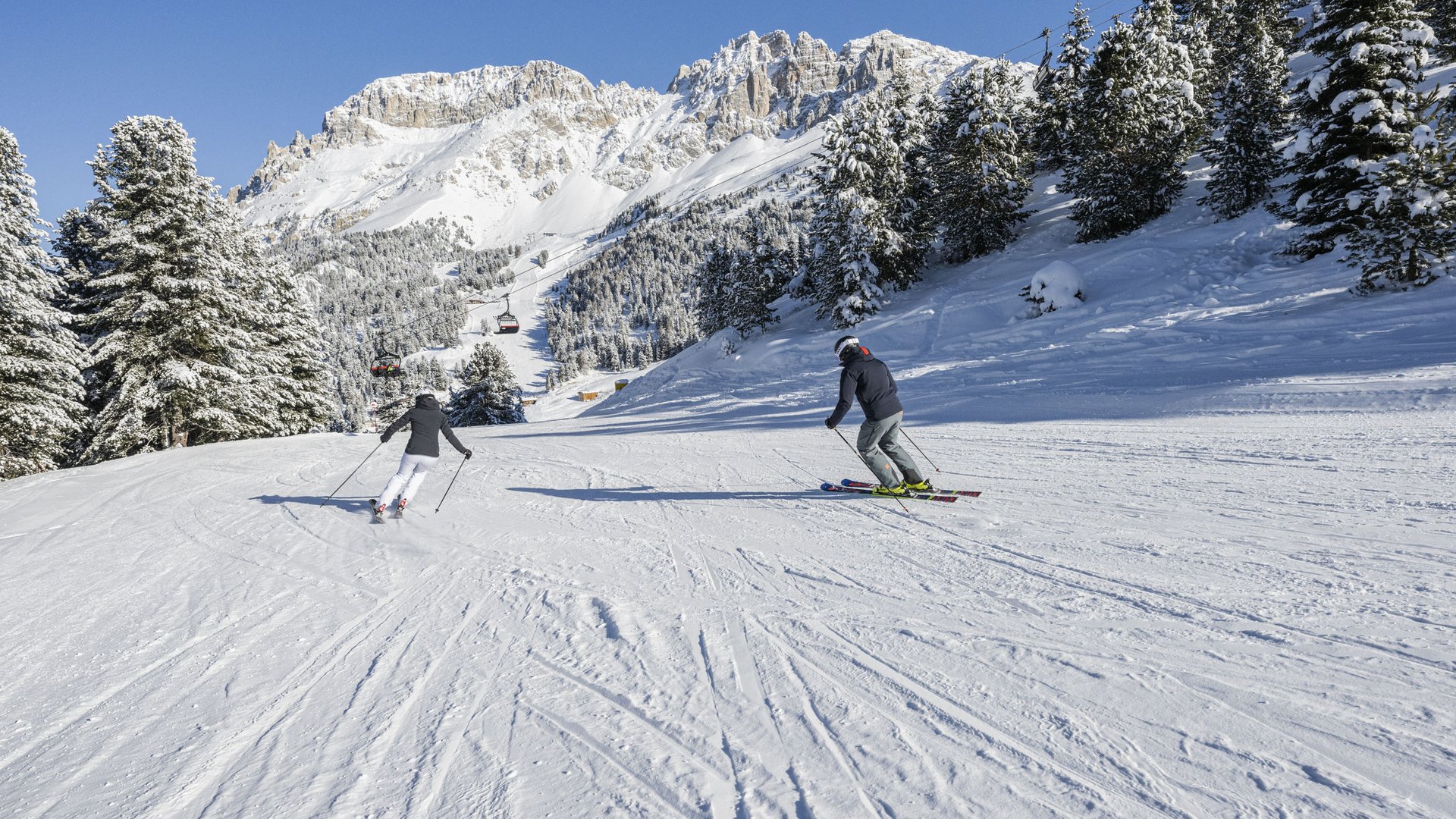 Settimana bianca sulle Dolomiti: inverno in Val d’Ega Due sciatori su pista innevata con montagne e alberi sotto un cielo limpido